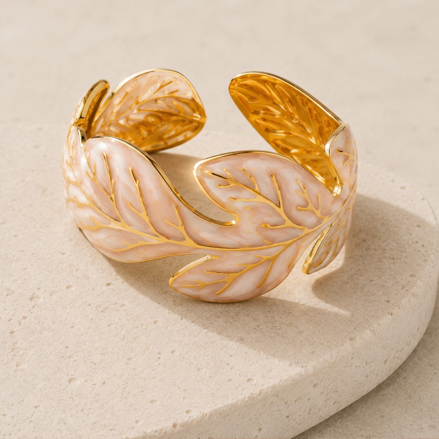 Una pulcera tipo cuff con diseño de hoja en tono dorado y detalles nacar en stainless steel con 18k gold plated
