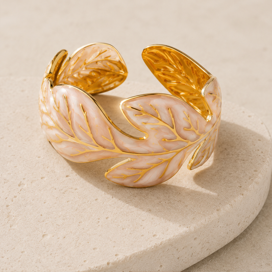 Una pulcera tipo cuff con diseño de hoja en tono dorado y detalles nacar en stainless steel con 18k gold plated